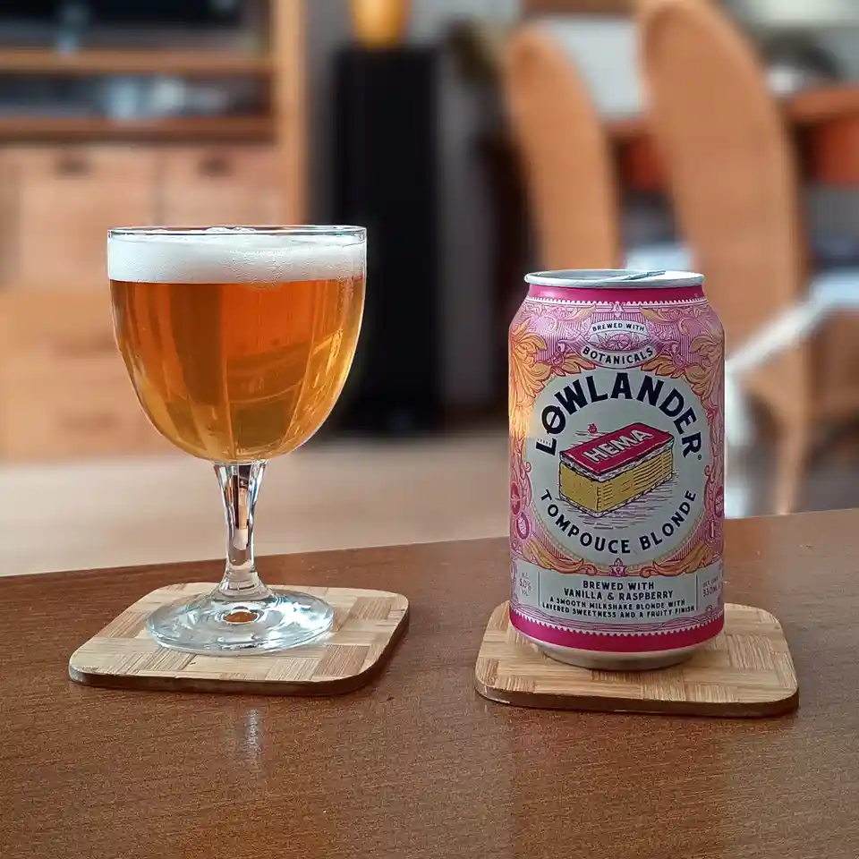 A can of Lowlander Tompouce Blonde beer, featuring a pink and gold label with an illustration of a HEMA brand butter block…