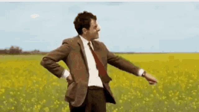 A man in a brown suit and red tie stands in a field of yellow flowers, then progressively becomes more overwhelmed…