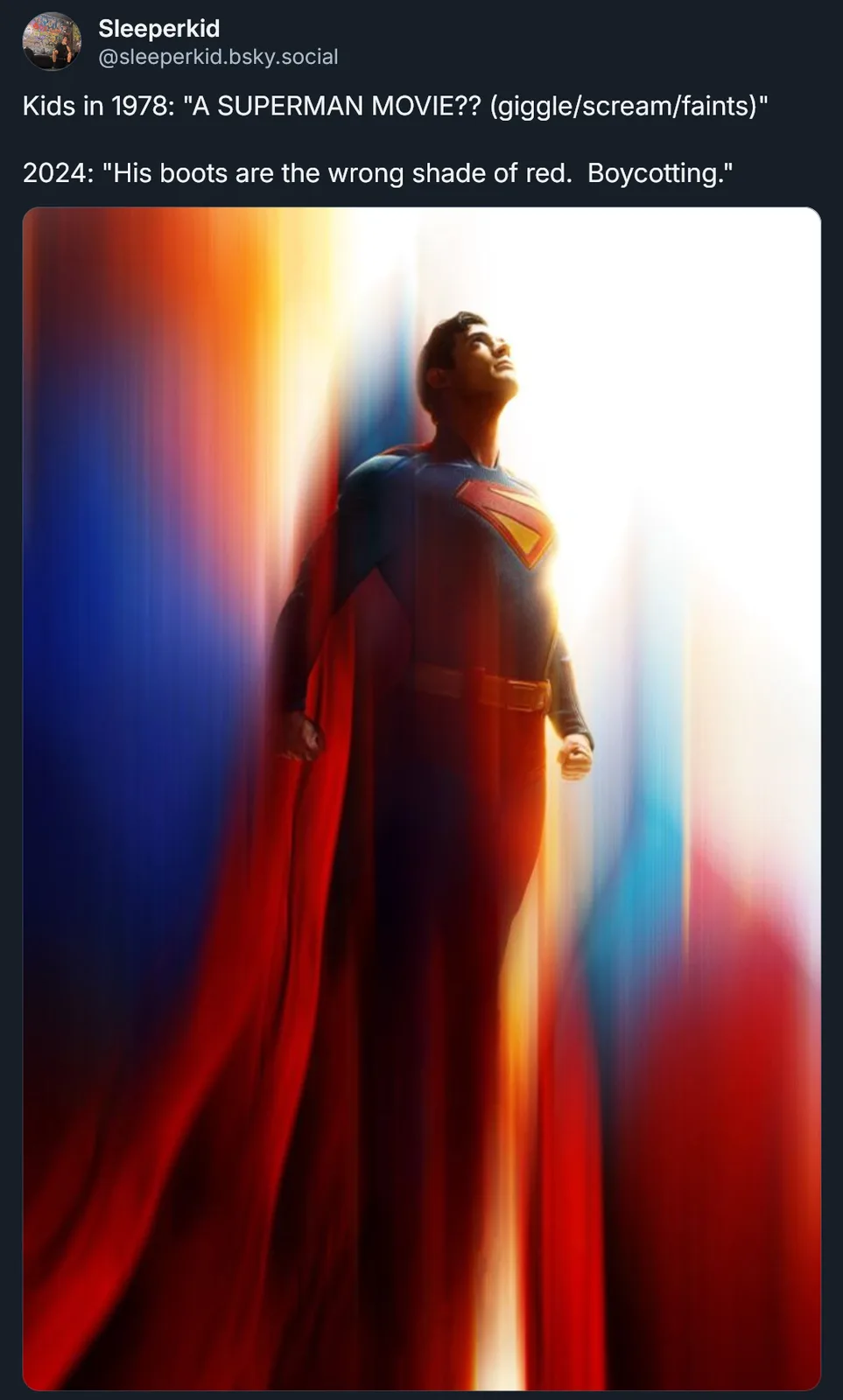 The image shows a man in a Superman costume standing with his head tilted up, bathed in bright, colorful light streaks. The…