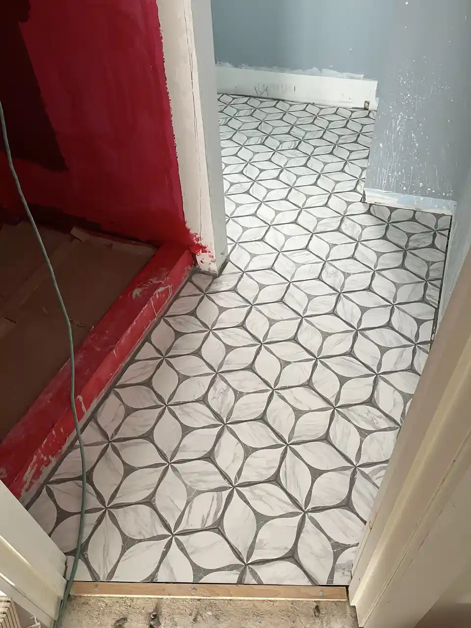 A photo shows a newly installed white and grey patterned tile floor in a room under renovation, with adjacent walls painted…