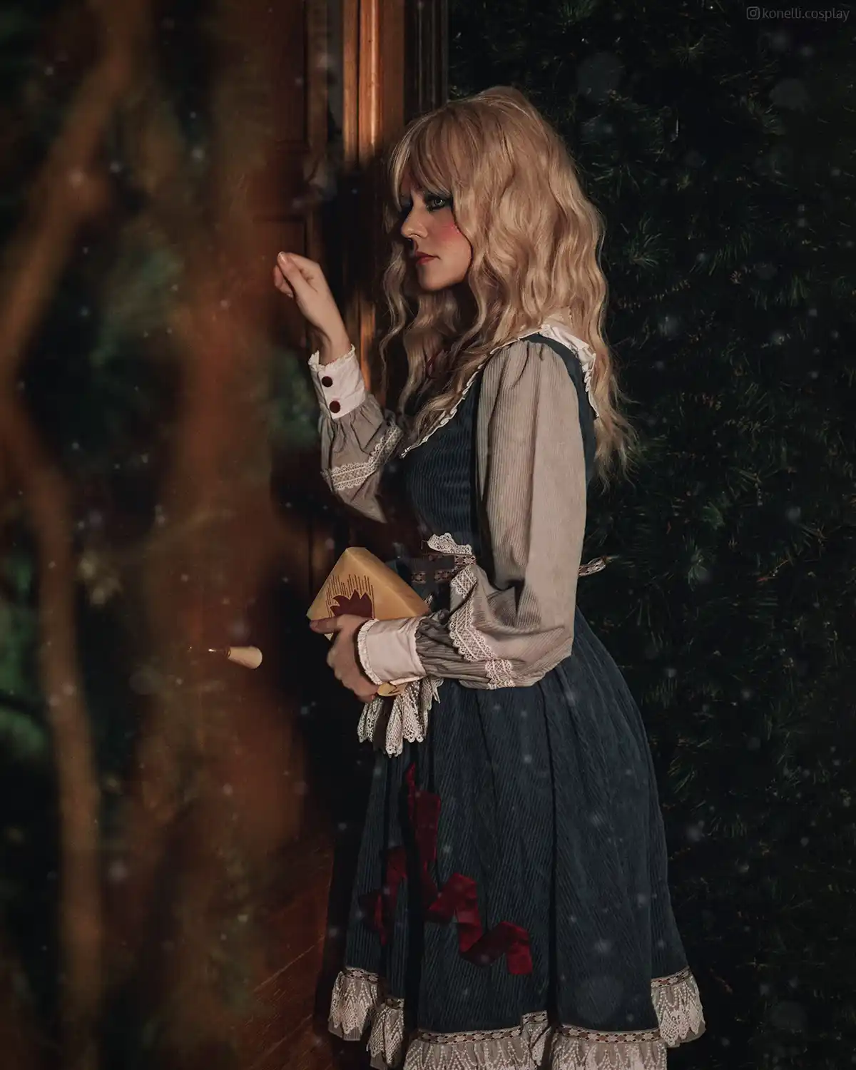 A person in a detailed, vintage-style dress with lace and red ribbon accents stands in a snowy, dimly lit setting near a…