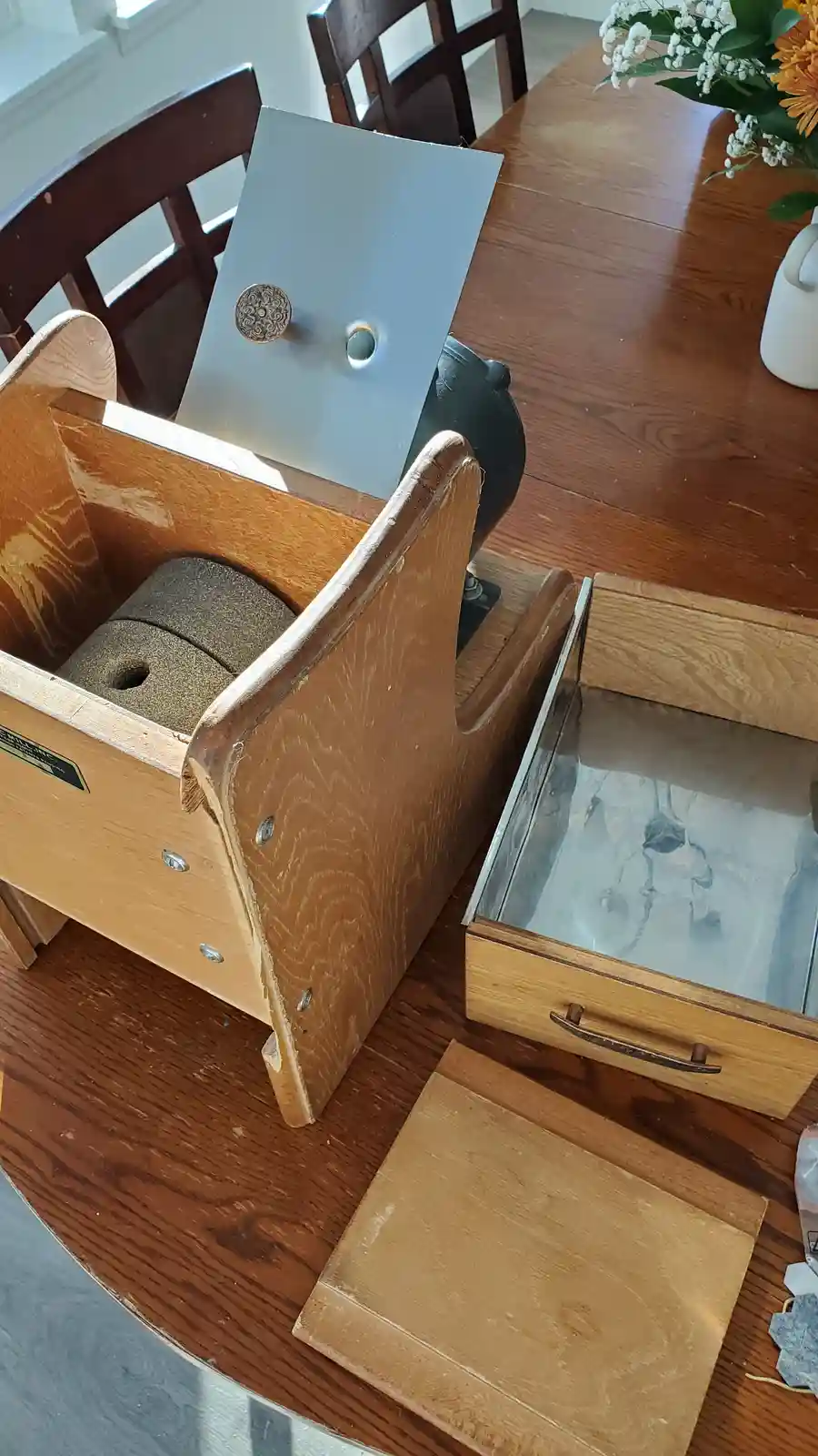 A disassembled vintage wooden and metal device, possibly a manual coffee grinder or similar appliance, sits on a wooden…