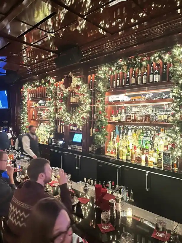 a warmly lit bar decorated with extensive christmas wreaths and garlands adorned with red and gold ornaments, surrounding…