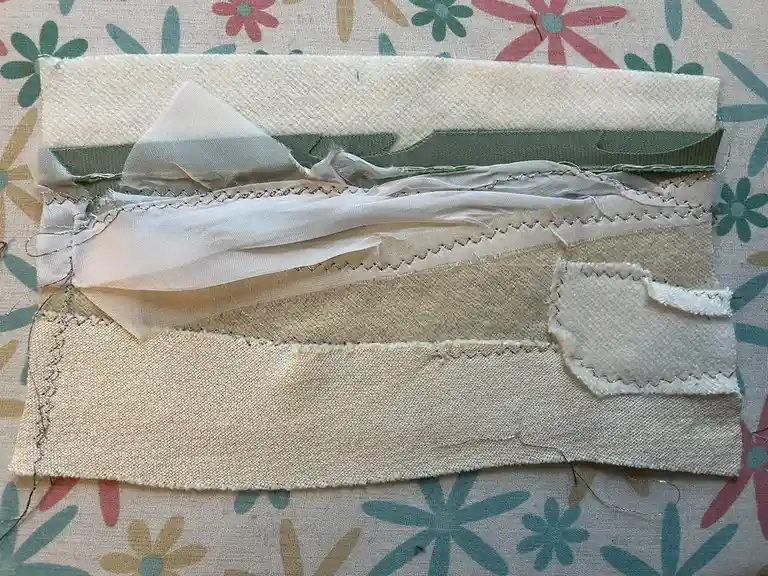 A close-up photo shows a patchwork of various fabric scraps, including beige, green, and sheer white pieces, stitched…