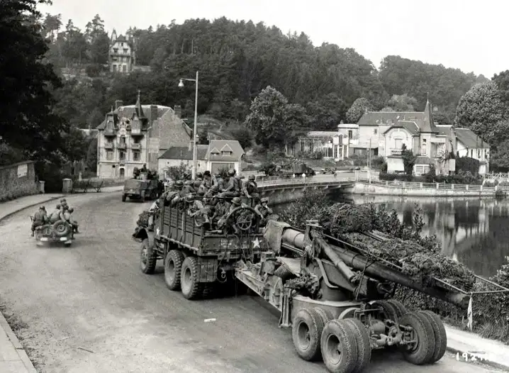 a black-and-white historical photo shows a convoy of military vehicles, including a large artillery piece and trucks…