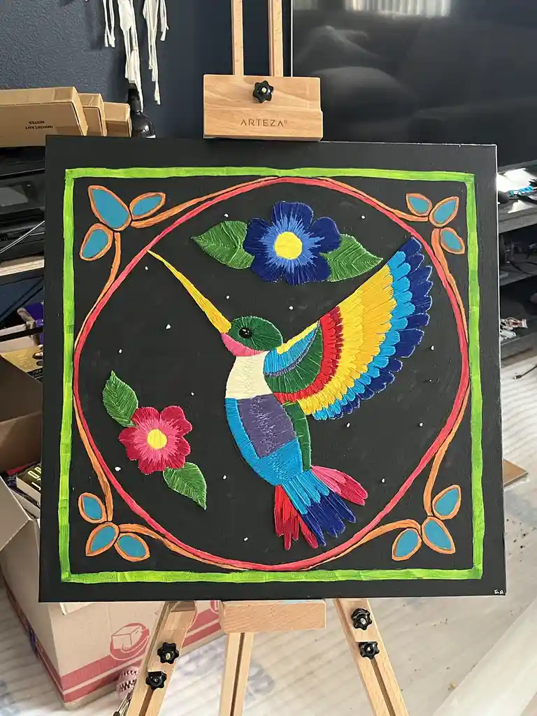 A colorful painting of a hummingbird with rainbow feathers and flowers on a black background, framed by a red circle and…