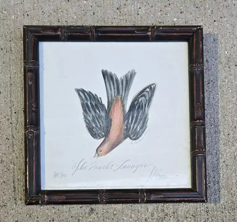 A framed painting of a bird with black wings and a reddish-orange body, labeled 'The Scarlet Tanager,' lies on a concrete…