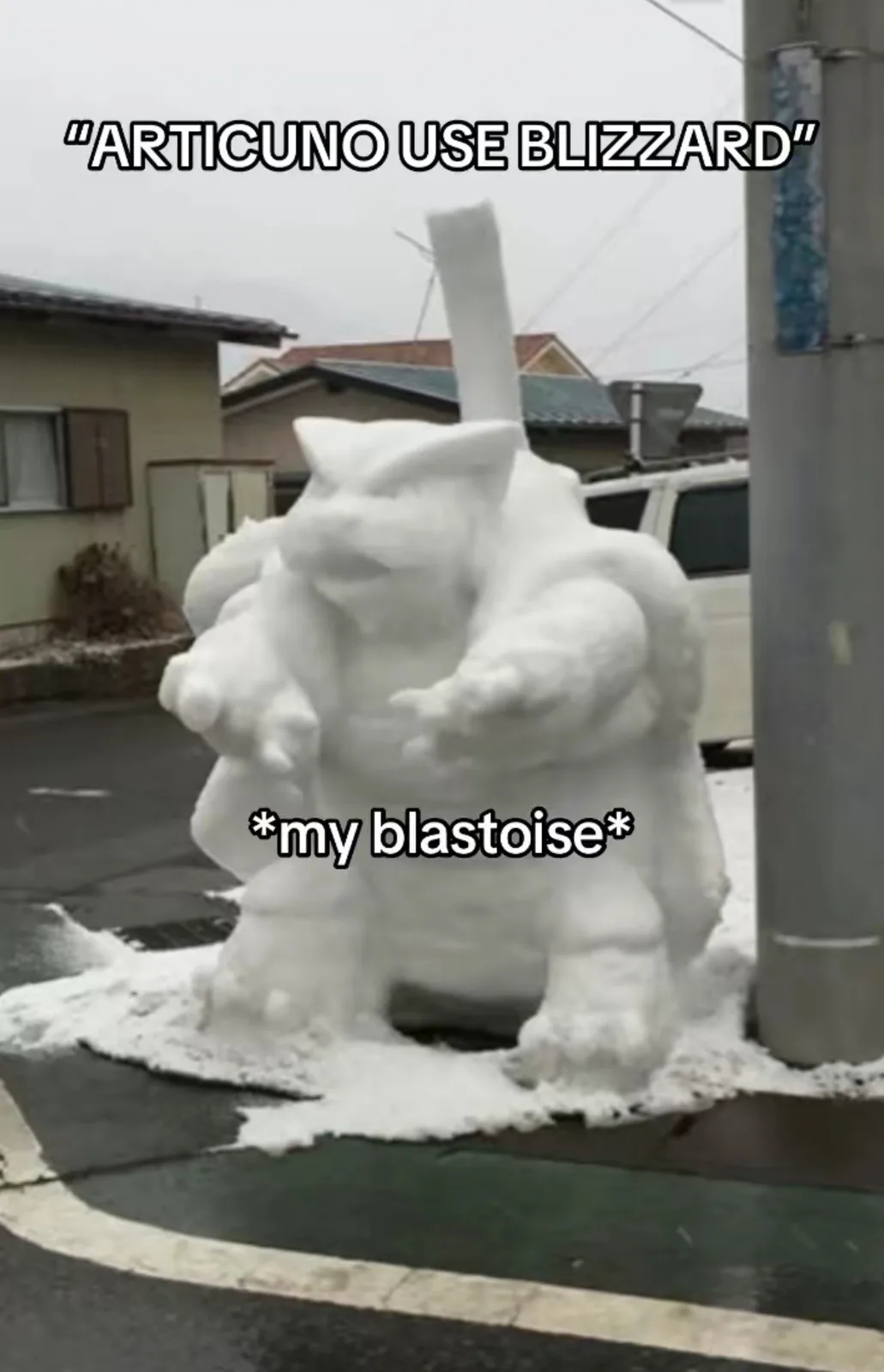 A large, crudely sculpted snow figure resembling the Pokémon Blastoise stands on a street corner, with a long snow pipe…