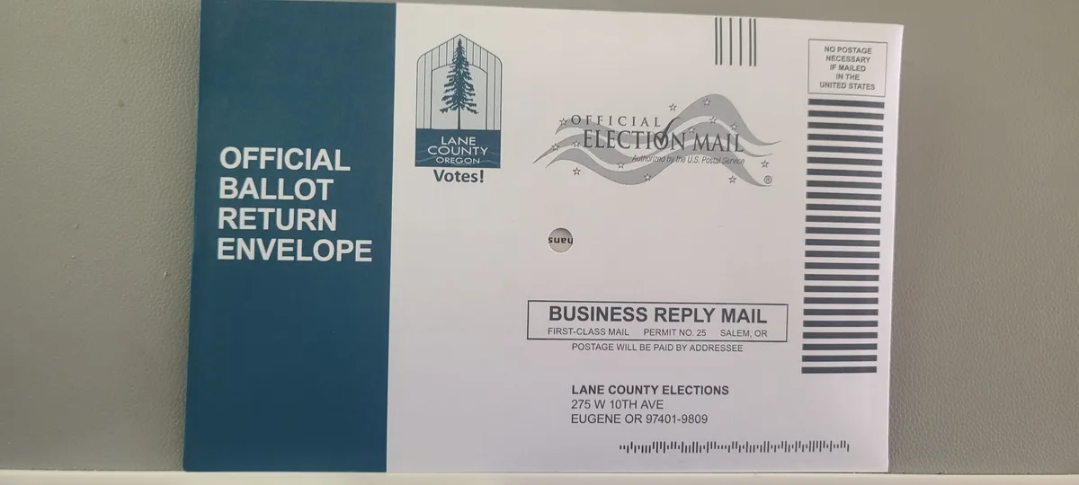 A close-up photo of an official Lane County, Oregon ballot return envelope, which is a business reply mail item with postage…