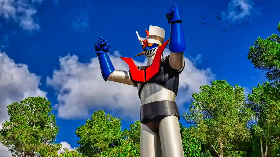 A large outdoor statue of the Japanese anime robot hero, Astro Boy, stands tall with both fists raised against a bright blue…