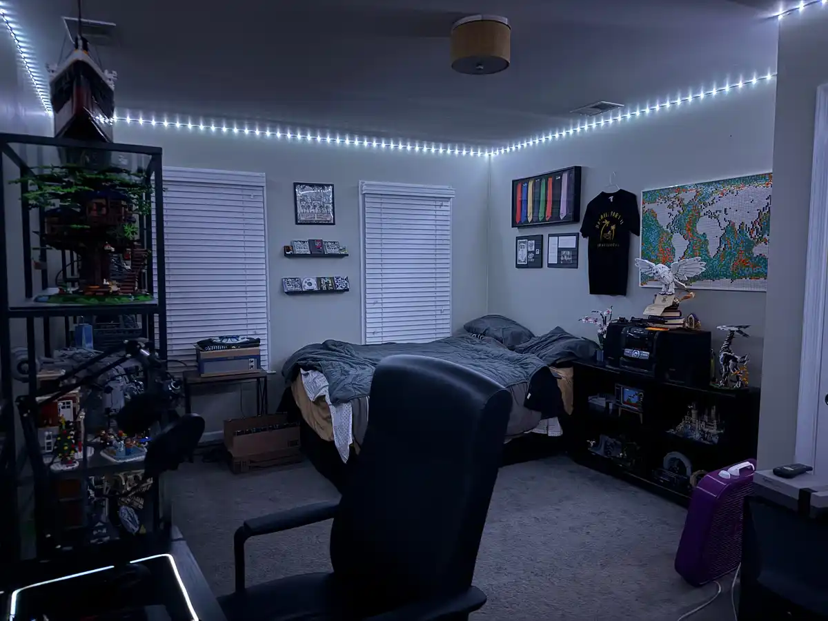 A dimly lit bedroom with white walls, a bed with a gray comforter, and a black office chair in the foreground. The room is…