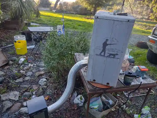 An outdoor setup features a large, mesh-covered smoker box with a black silhouette of a person holding a smoking pipe drawn…