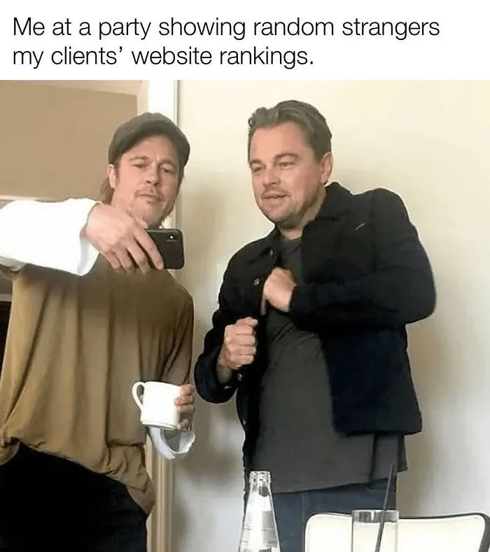 Two men are pictured, one holding a phone as if showing something to the other, who reacts with a look of mild surprise or…