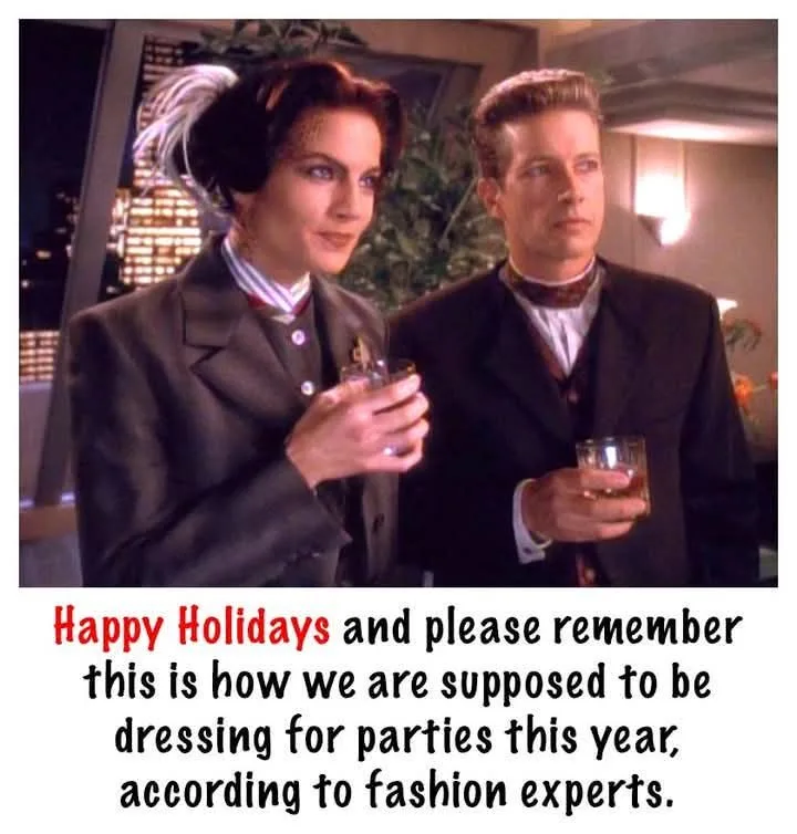 A still from a TV show shows a woman in a dark suit with a feathered hair accessory and a man in a dark suit with a bow tie…