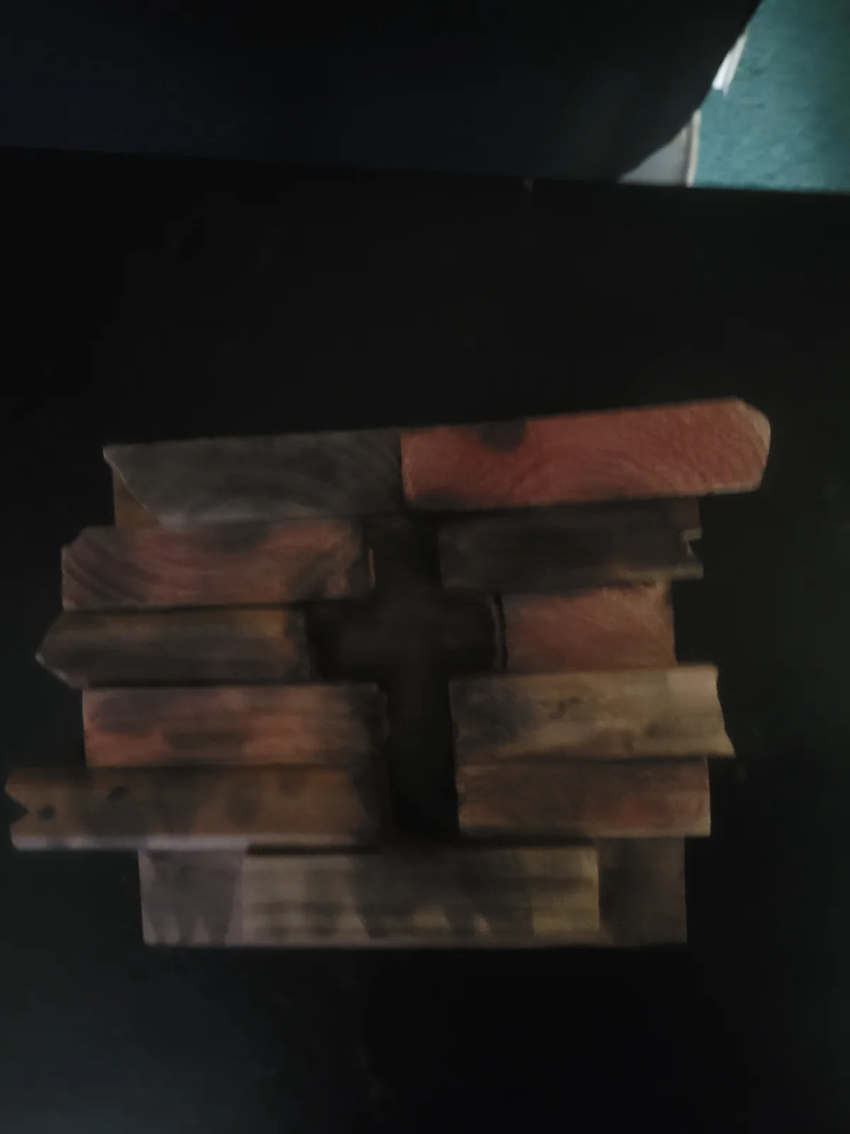 A dark, blurry photo shows several rough wooden planks arranged on a black surface to form the shape of a swastika. The wood…