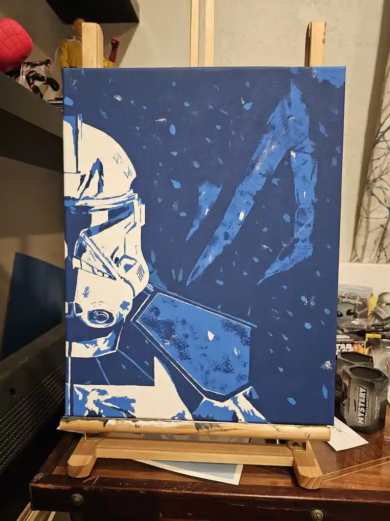 A hand-painted canvas on an easel depicts a stylized white stormtrooper helmet and torso against a blue background with…