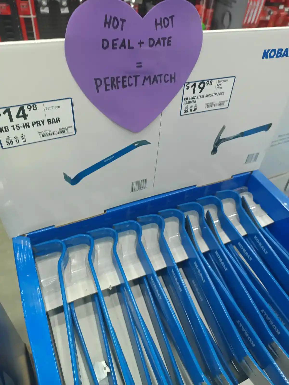 A purple heart-shaped sign taped to a store display box for Kobalt tools reads 'HOT HOT DEAL + DATE = PERFECT MATCH'. Below…