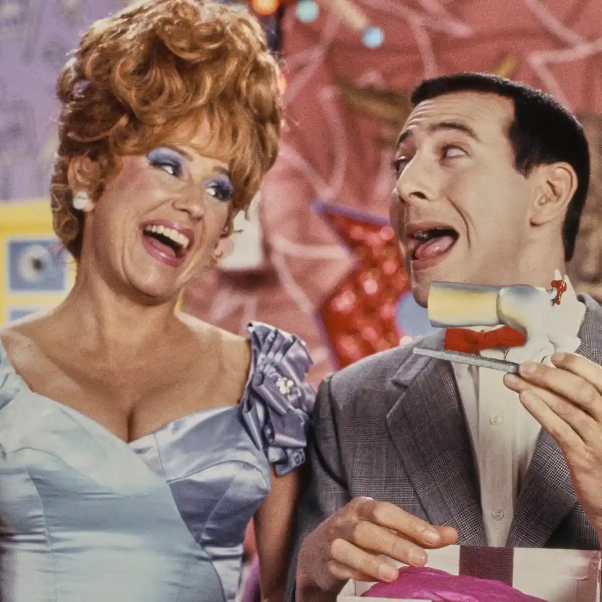 A man in a suit holds a cake knife and looks upward with a shocked expression, while a woman in a light blue dress laughs…