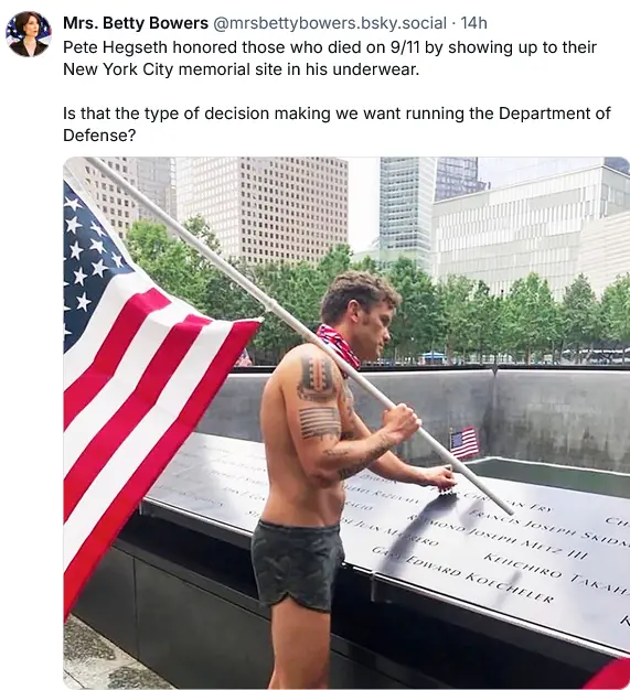 A shirtless man in camouflage underwear stands at the 9/11 Memorial in New York City, holding an American flag pole. He has…