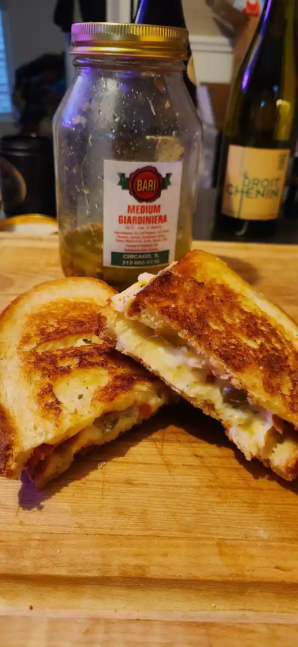 A close-up photo shows a golden-brown, grilled cheese sandwich cut in half on a wooden cutting board, revealing melted…