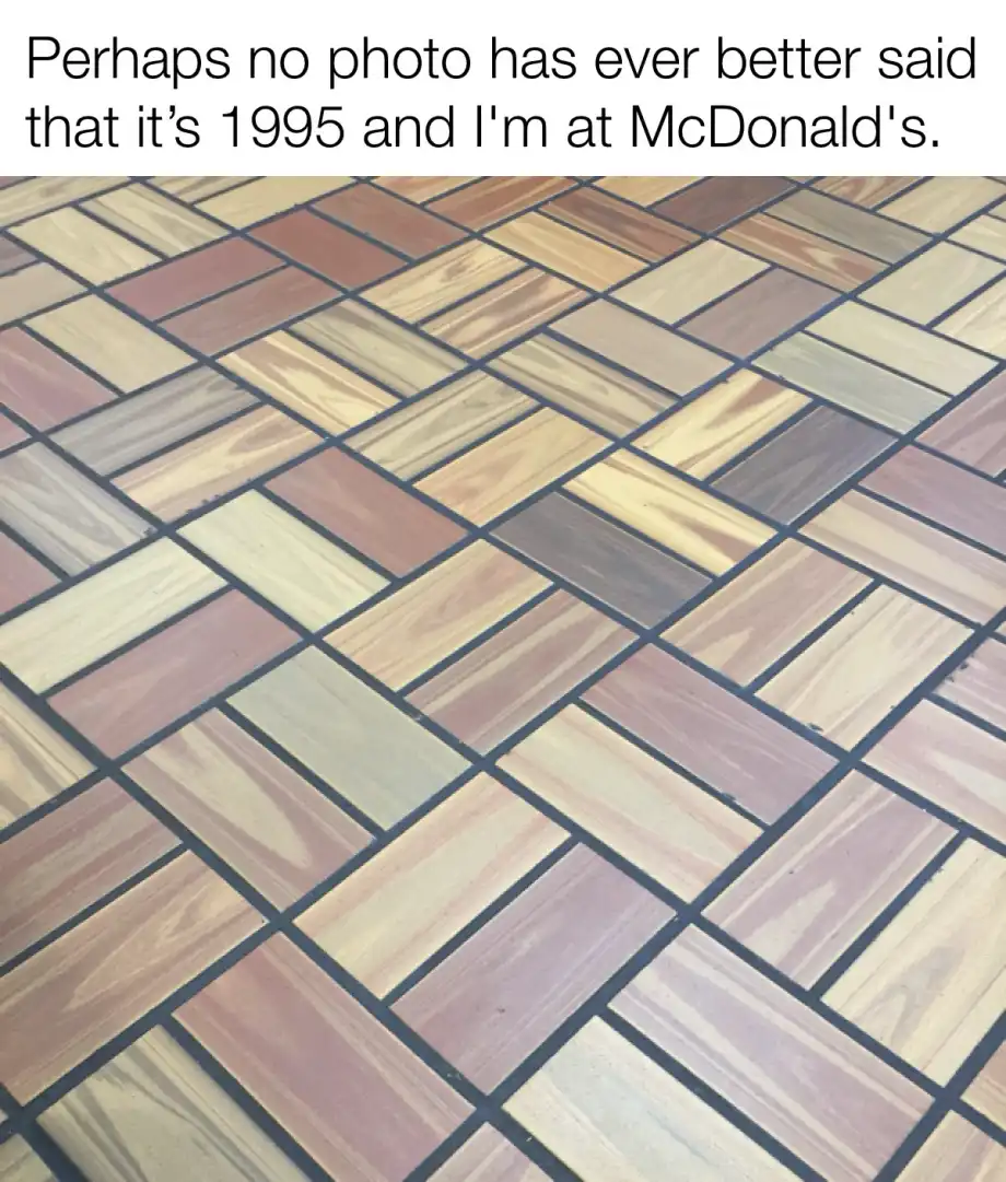 A close-up photo of a floor made of rectangular tiles arranged in a herringbone pattern, featuring various shades of wood…