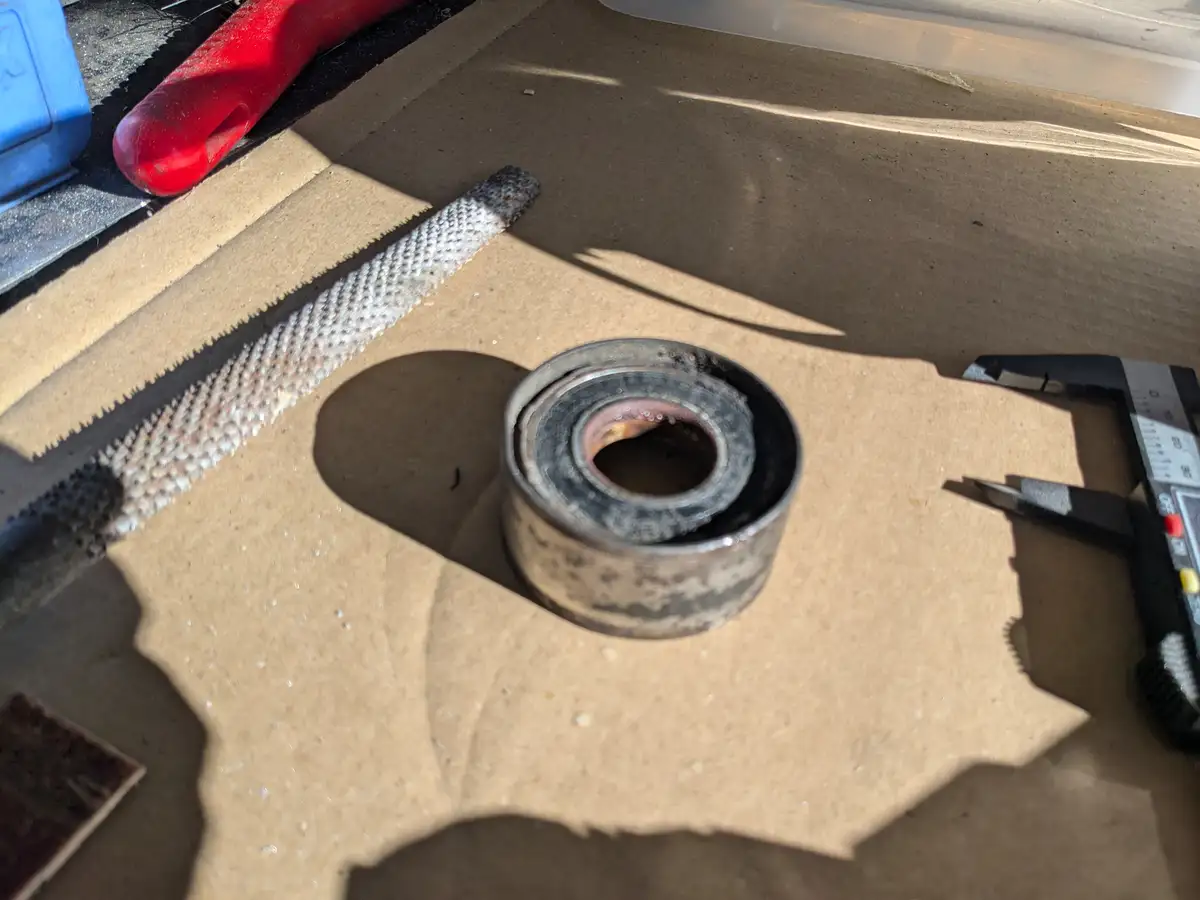 A close-up photo shows a worn, dirty cylindrical metal bearing resting on a cardboard surface, surrounded by tools including…