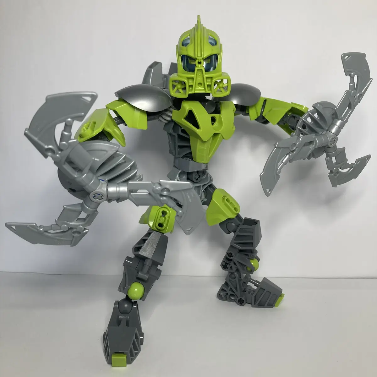 A lime green and gray Bionicle action figure stands in a dynamic pose against a plain white background, its articulated…