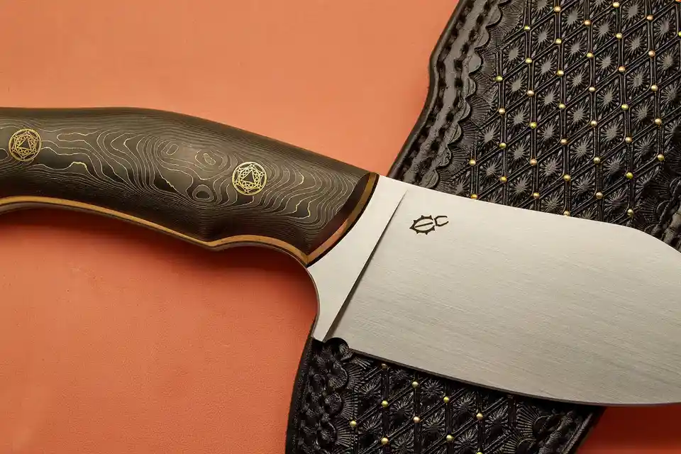 A close-up photograph of a high-end custom knife with a dark, wood-grain patterned handle featuring gold inlays and a sleek…