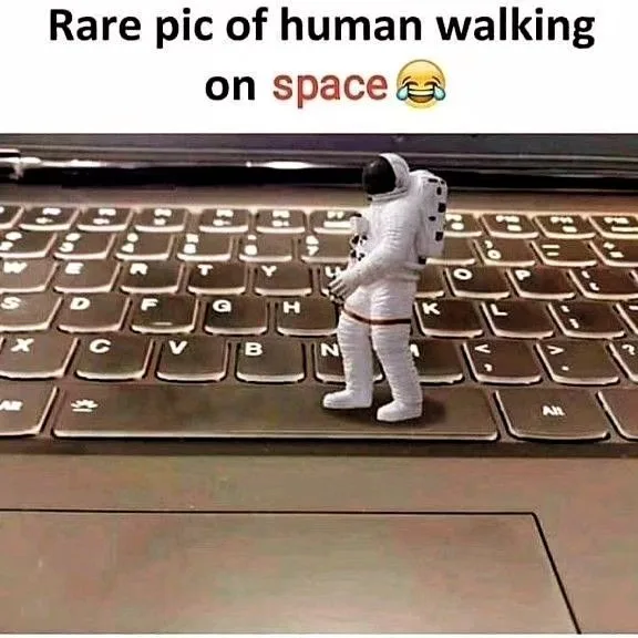 A tiny astronaut figurine stands on a laptop keyboard, humorously labeled as a 'rare pic of human walking on space' with a…