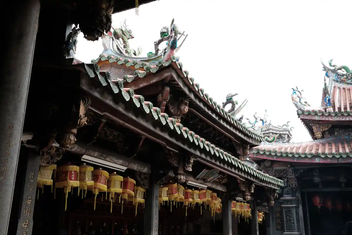 An ornate traditional Chinese temple roof with colorful dragon sculptures and green-tiled edges, featuring rows of hanging…