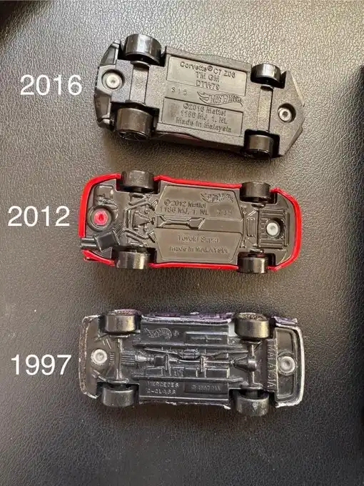 Three Hot Wheels toy cars are shown upside down on a dark surface, each labeled with a year: 2016 (top), 2012 (middle), and…