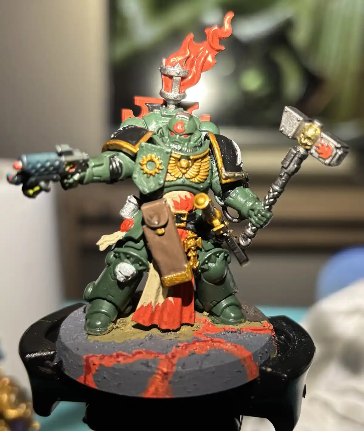 A close-up photo of a green-painted, heavily armored miniature warrior figurine, likely from Warhammer 40,000, standing on a…
