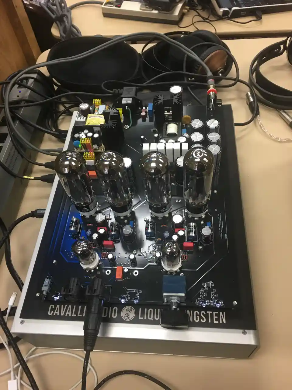 A close-up photo of a high-end, silver-and-black tube amplifier labeled 'CAVALLI AUDIO LIQUID TUNGSTEN' with six glowing…