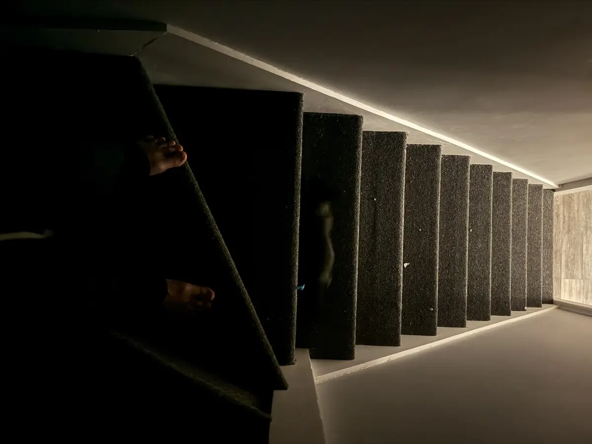 A low-angle shot shows a person's bare feet and legs descending a dimly lit staircase with dark carpeted steps. The scene is…