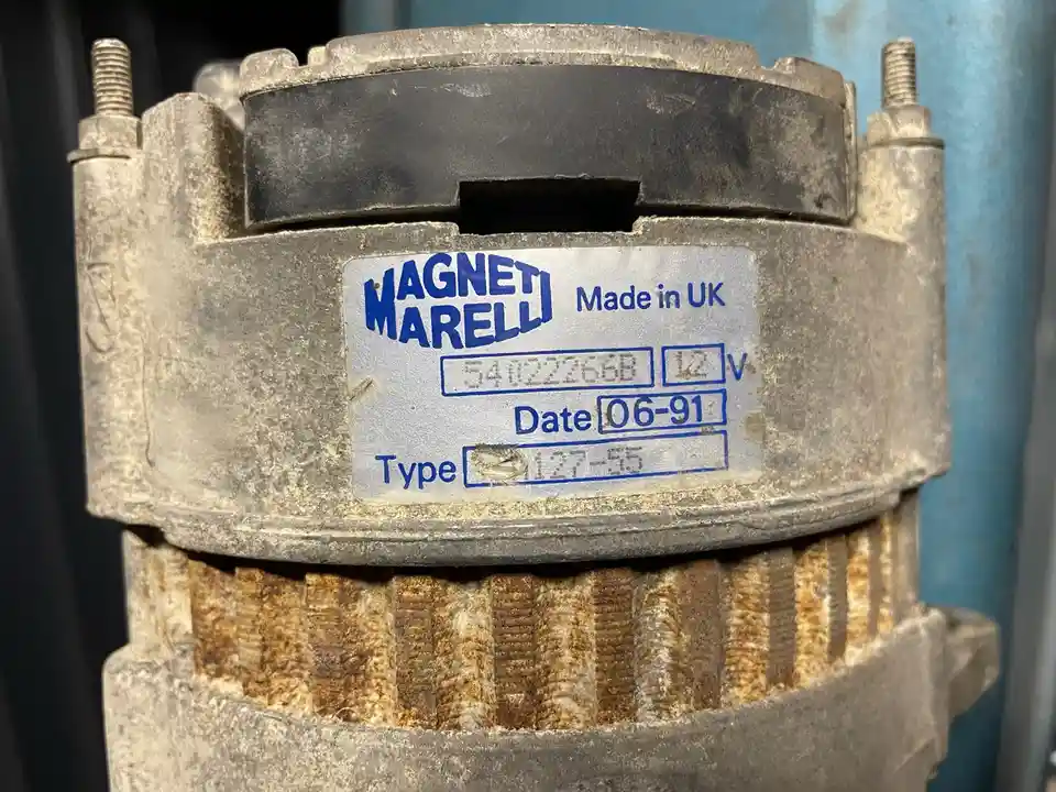 A close-up of a rusty, weathered automotive alternator with a label showing 'MAGNETI MARELLI Made in UK', serial number…