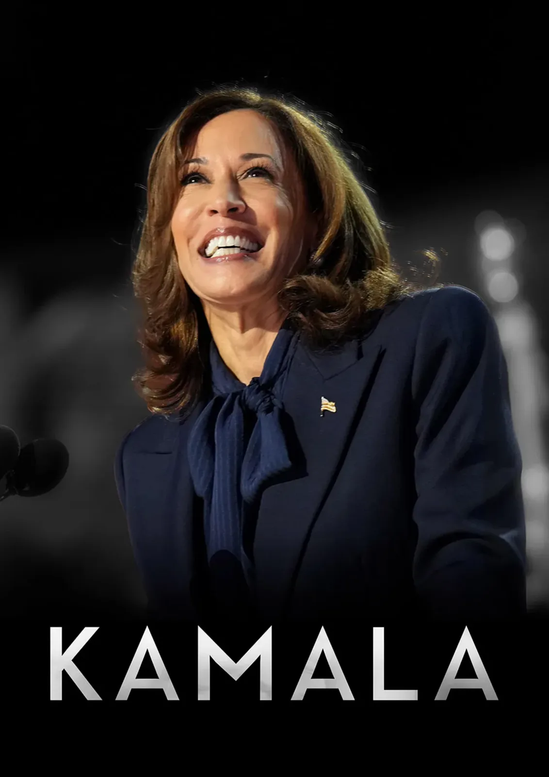 A close-up photo of Kamala Harris smiling broadly while speaking at a podium, wearing a dark blue suit with a bow tie and a…