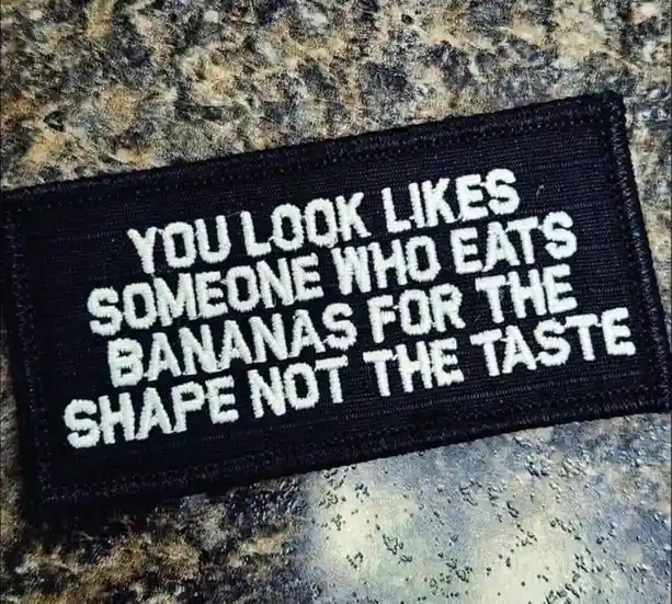 A black rectangular patch with white embroidered text reading 'YOU LOOK LIKES SOMEONE WHO EATS BANANAS FOR THE SHAPE NOT THE…