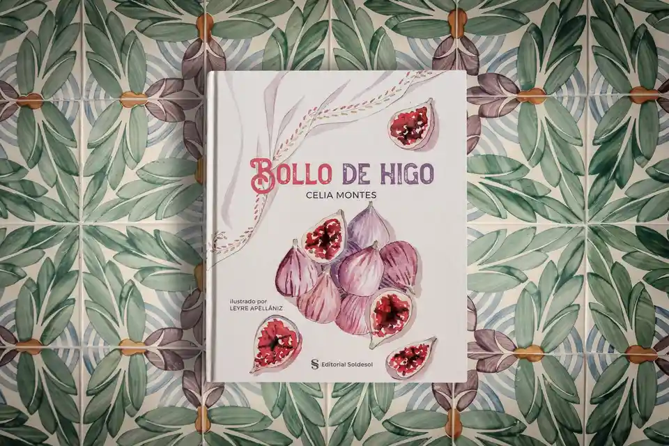 A cookbook titled 'Bollo de Higo' by Celia Montes, illustrated by Leyre Apellániz, rests on a patterned tile floor with…