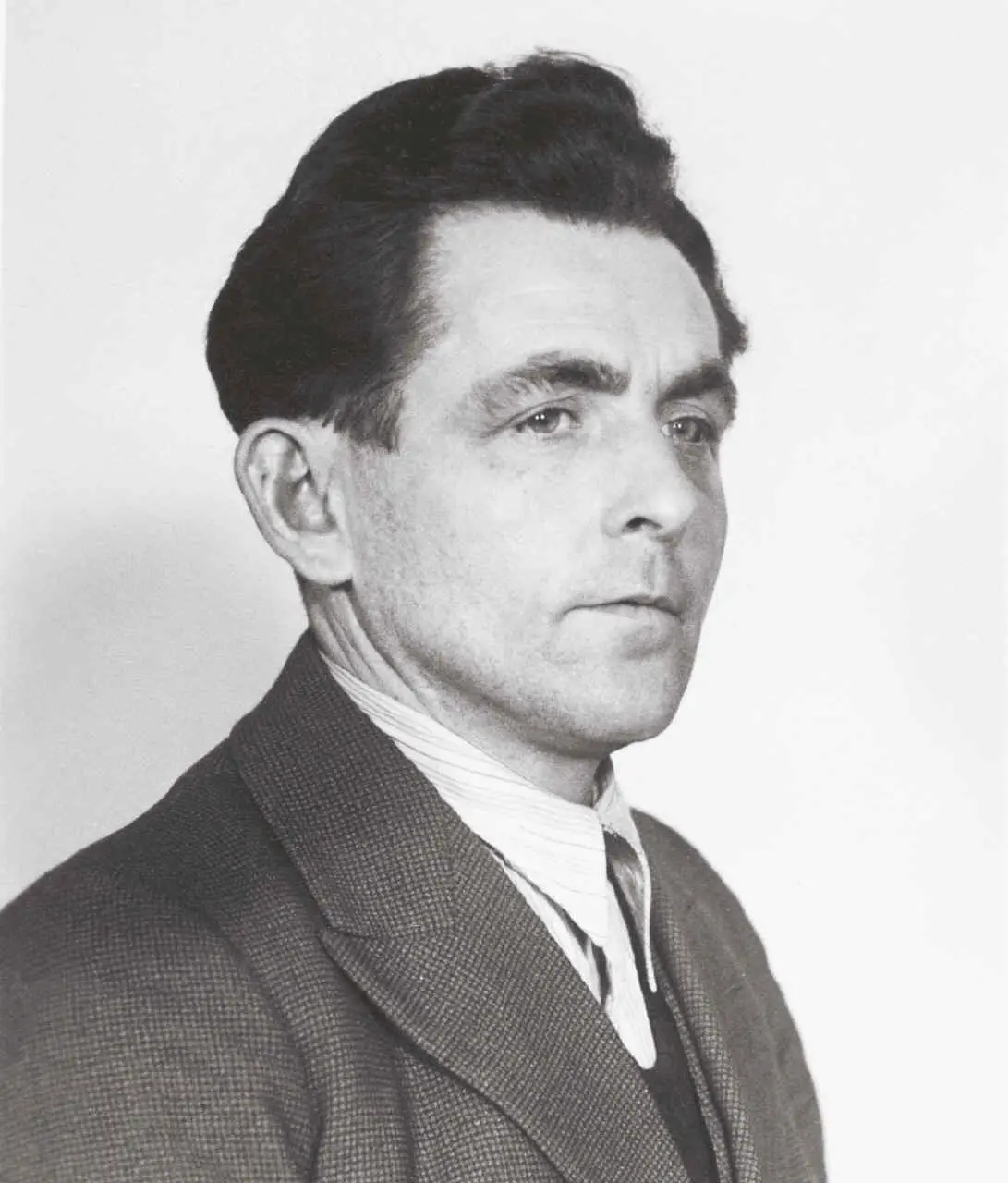 A black-and-white portrait of a man in a suit and tie, looking off to the side with a stern, unimpressed expression. The…