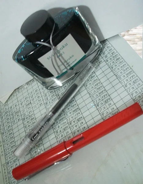 A glass bottle of blue ink labeled 'Shirokoku' sits atop a sheet of paper filled with Japanese hiragana characters…