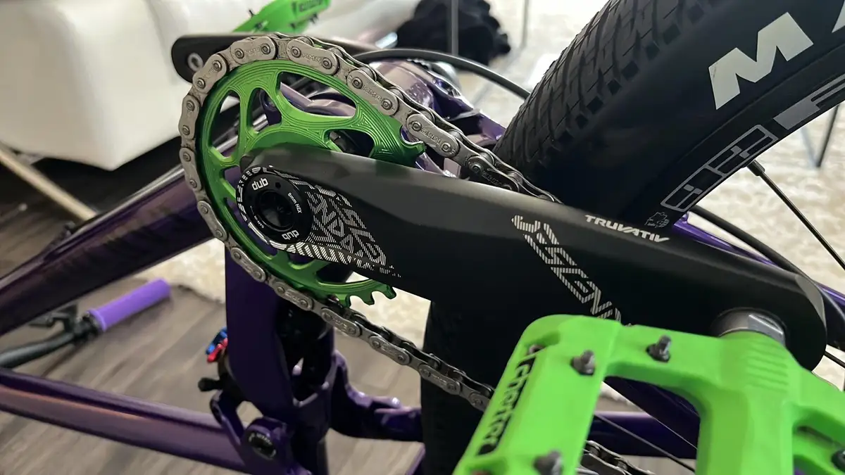 A close-up photo of a bicycle's drivetrain showing a bright green chainring, a black crank arm with 'TRUVATIV' branding, and…