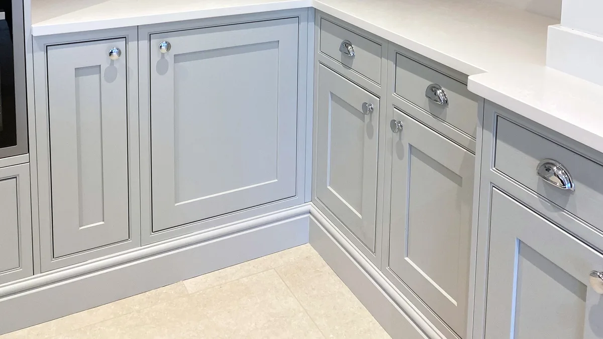 A photo of light gray kitchen cabinets with white countertops and chrome handles, showing a clean, modern kitchen corner…
