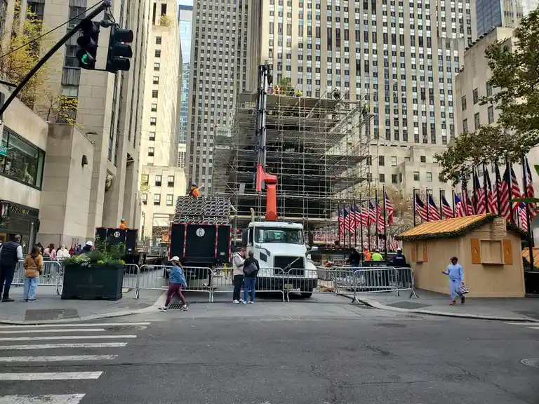A street view of Rockefeller Center in New York City, showing construction scaffolding on the iconic building, workers on…