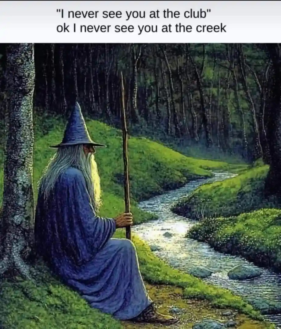 A painting depicts a wizard with a long white beard and blue robe sitting by a creek in a forest, holding a staff. The…