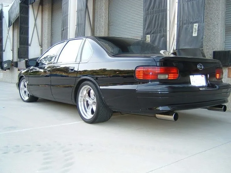 A glossy black sedan, likely a Nissan Altima, is parked outdoors with aftermarket chrome wheels, dual exhaust pipes, and a…