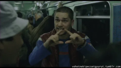 A man in a red vest and blue shirt on a crowded subway train makes increasingly frantic hand gestures while speaking to…