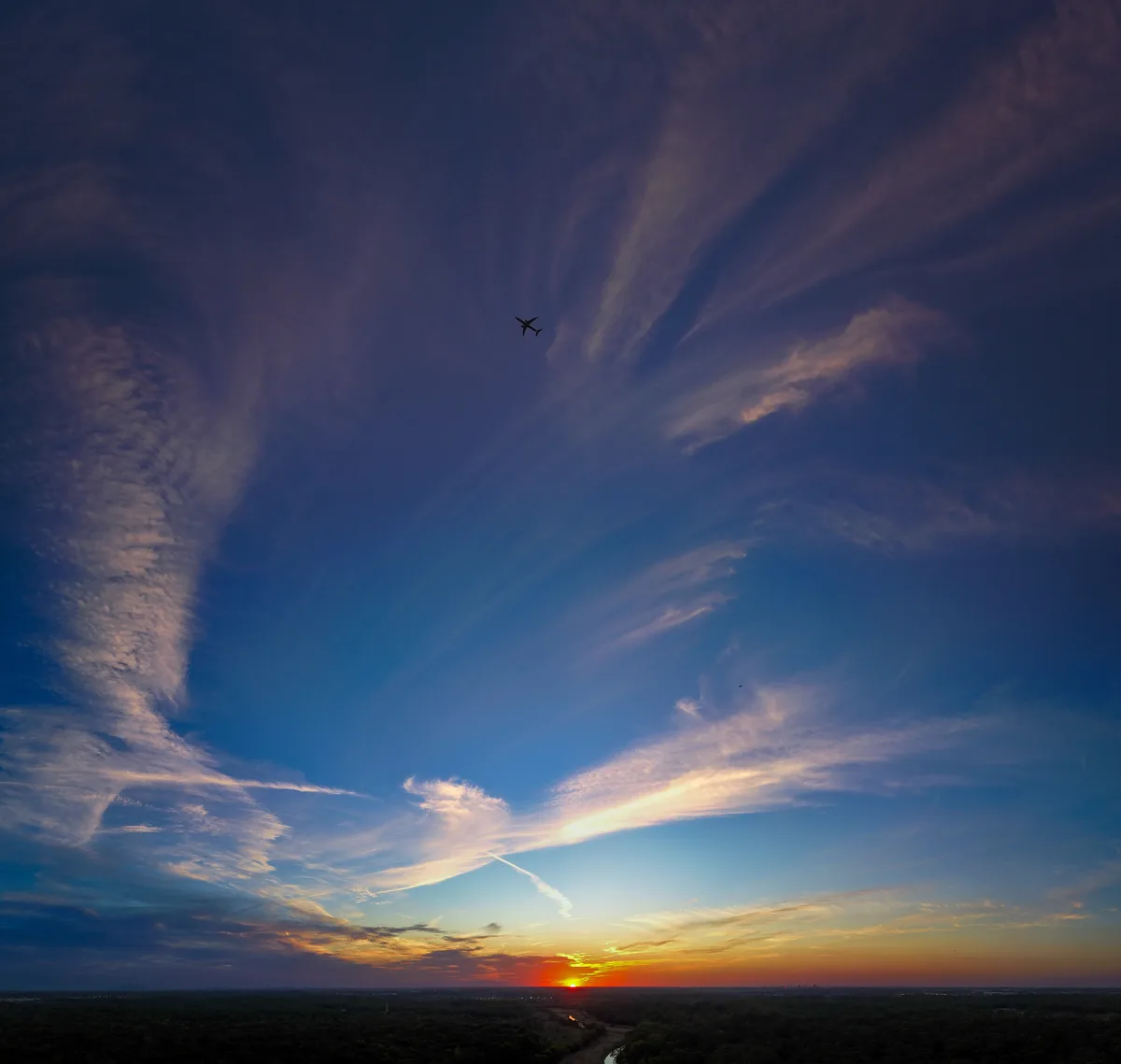 A serene sunset photograph shows a silhouetted airplane flying against a sky painted with streaks of purple, blue, and…