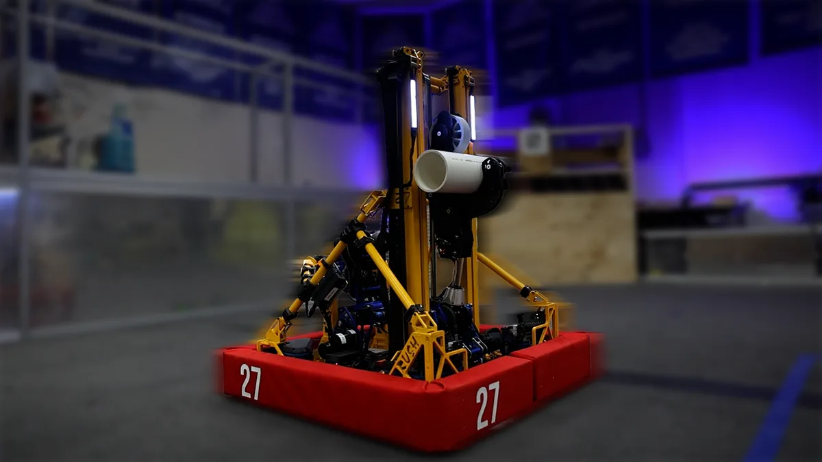 A yellow and black robot with a large white cup attached to its arm, mounted on a red base with the number 27 on both sides…