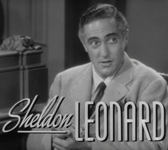 A black-and-white still of actor Sheldon Leonard, looking upward and to his right with a surprised or confused expression…