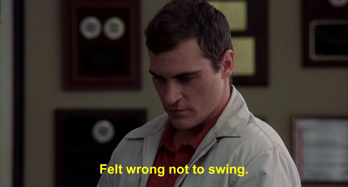 A man with dark hair, wearing a light-colored jacket over a red shirt, looks down with a serious, contemplative expression…